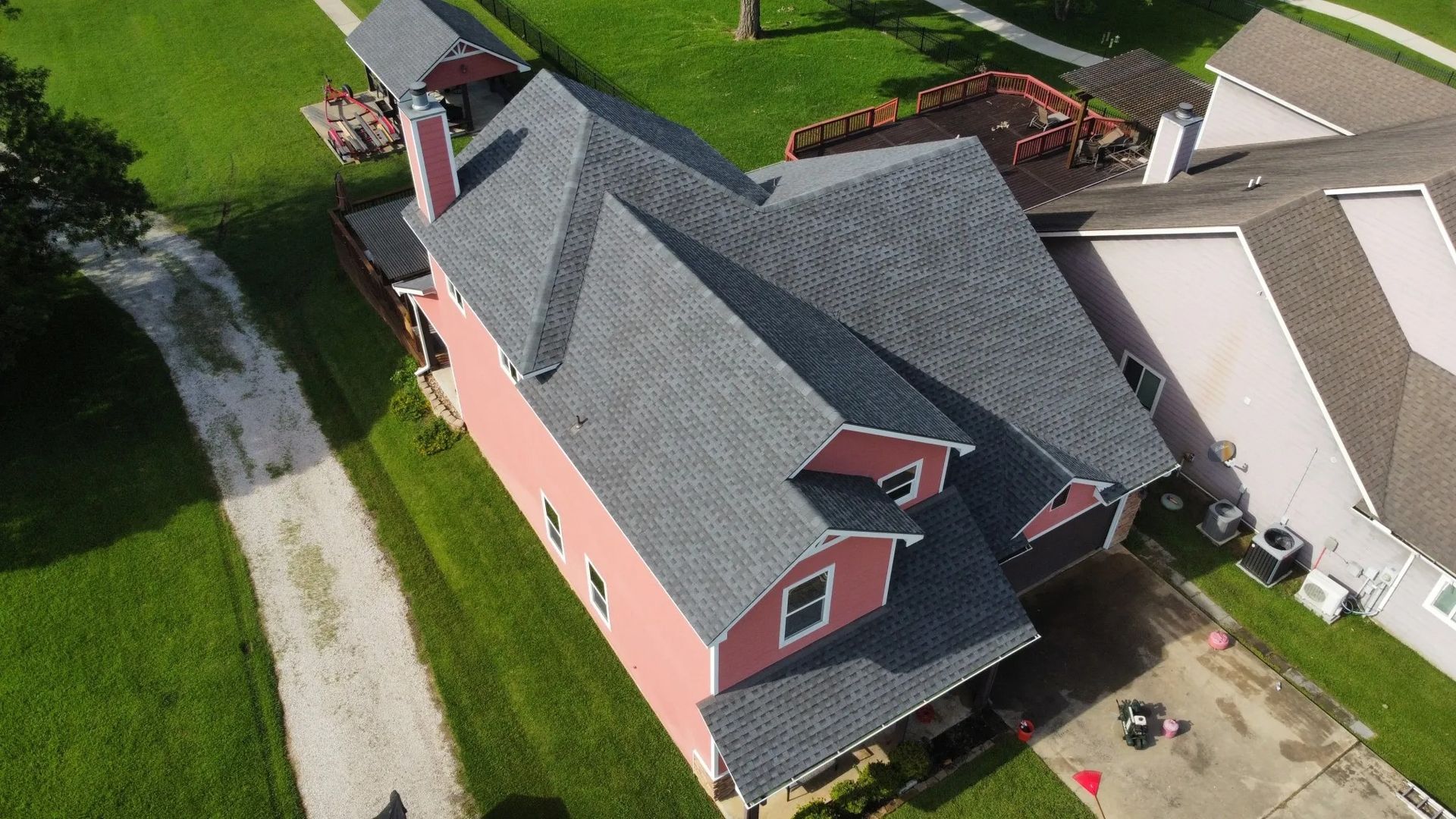 Aerial view of a red house with a gray roof beside a road and neighboring homes