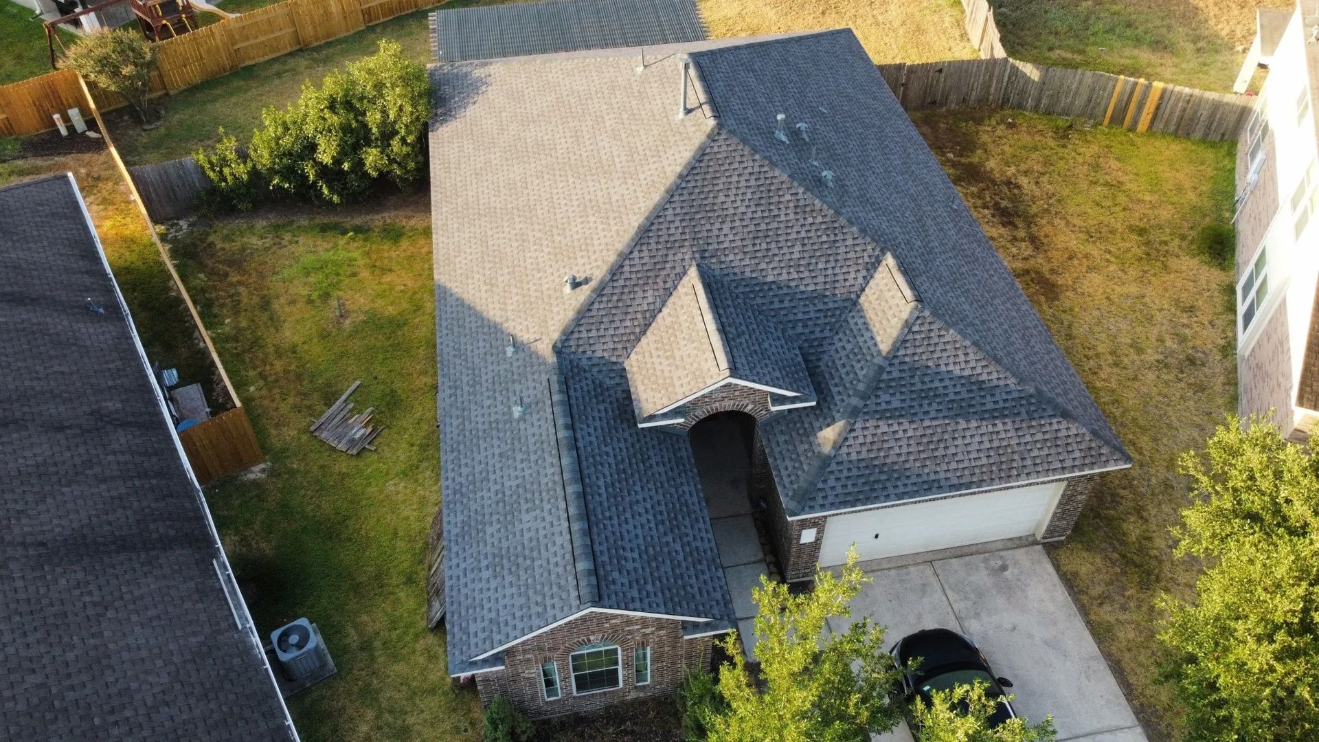 Aerial view of a suburban house with a gray roof, driveway, and surrounding green yard.