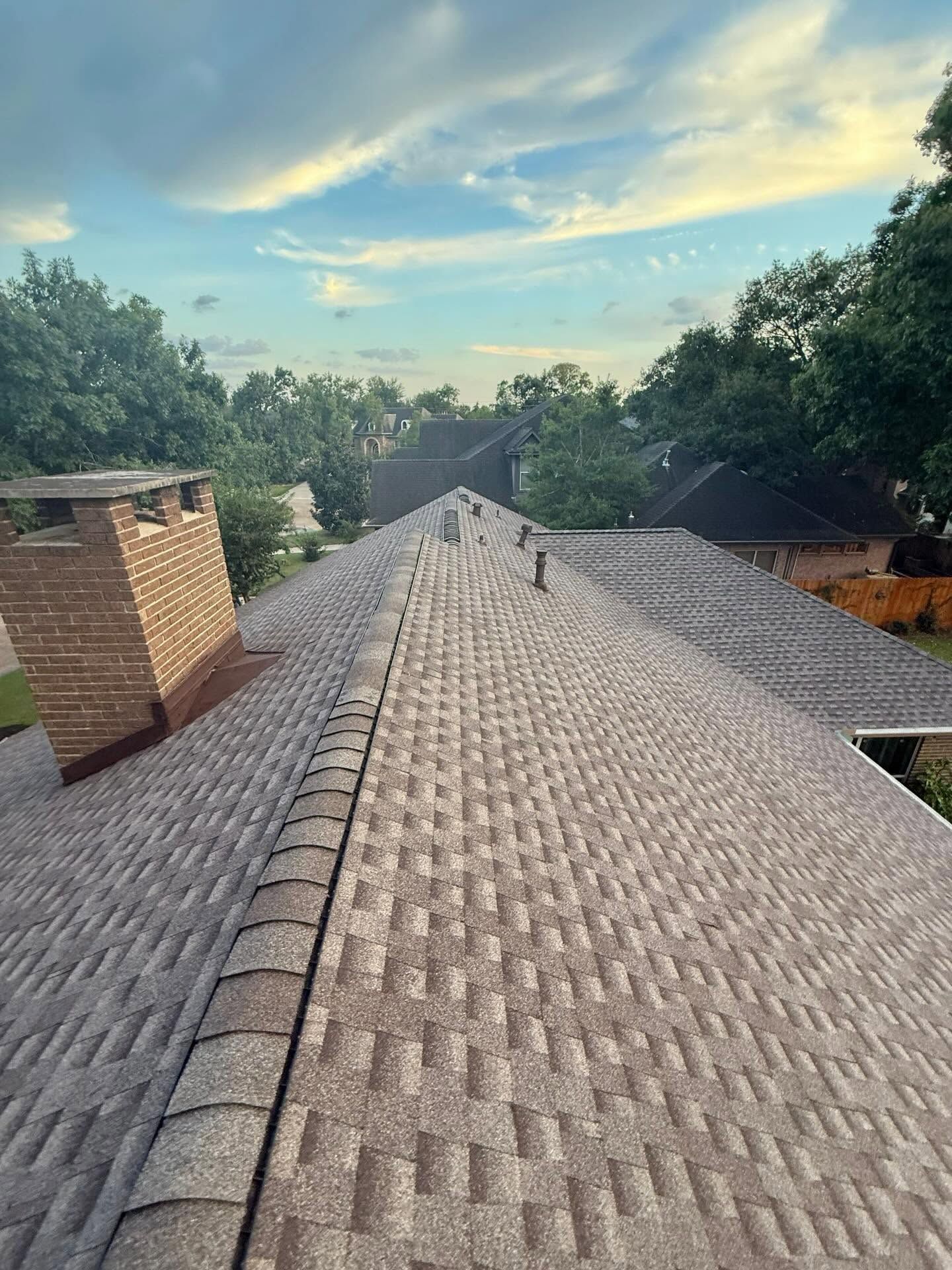 Rooftop with gray shingles and brick chimney under a partly cloudy sky, viewed from the ridge.