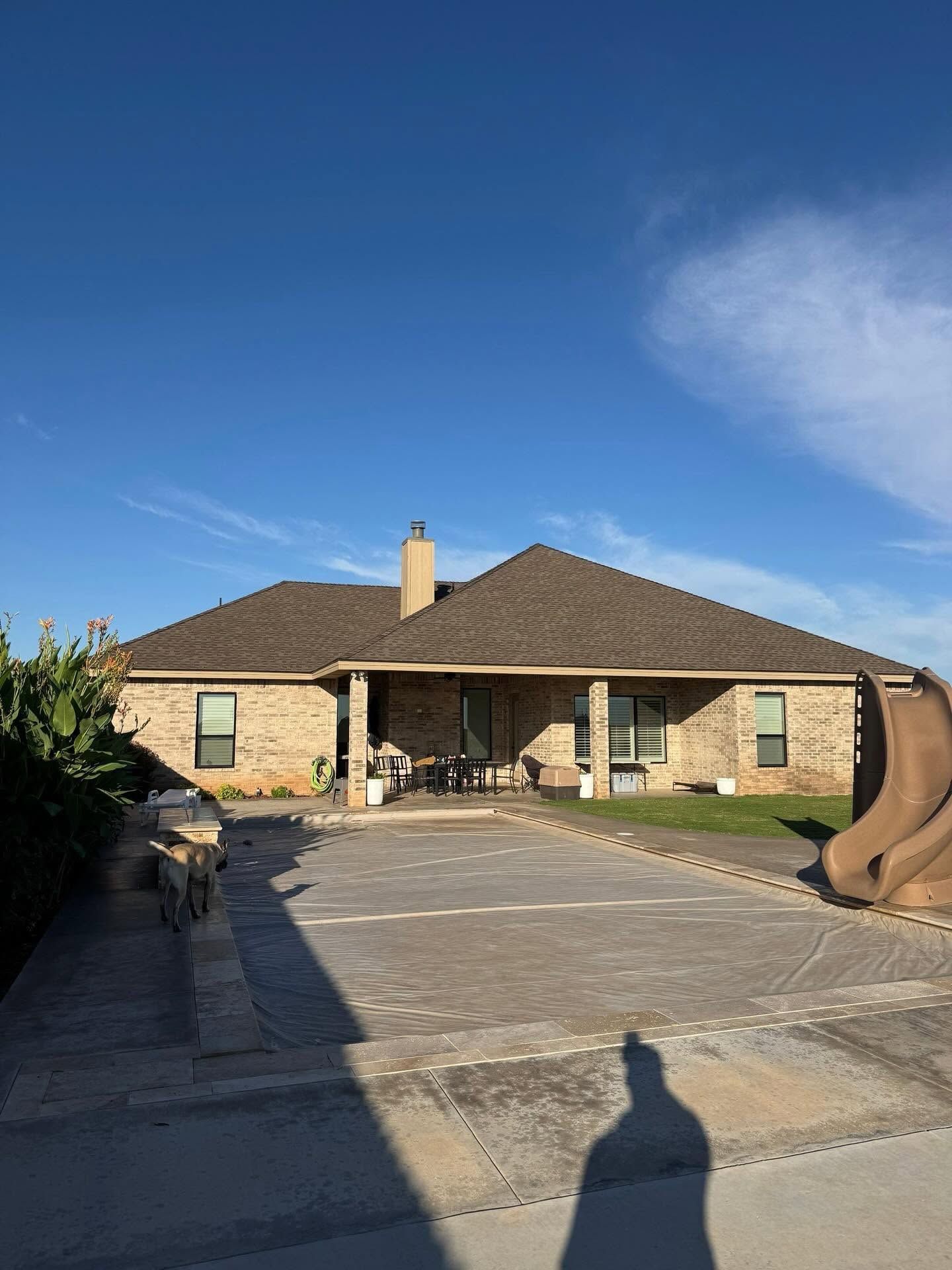 Single-story brick house with a tiled roof, stone driveway, and blue sky background
