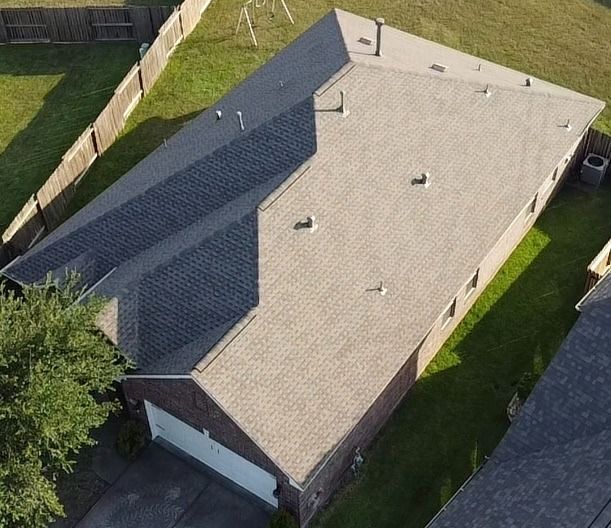 Aerial view of a gray-roofed house with a driveway and fenced yard.