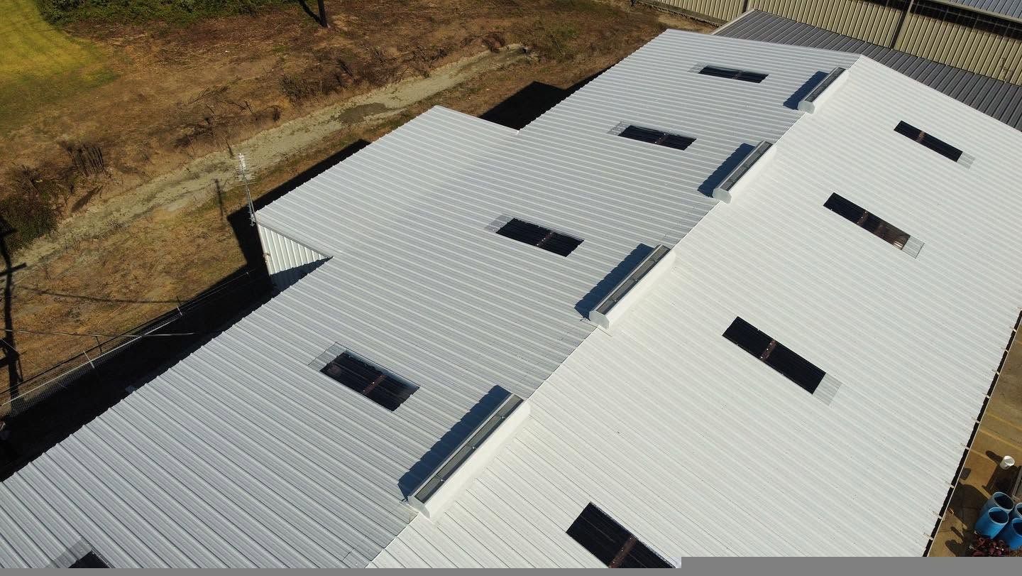 White metal roof with several skylights, viewed from above in a rural setting