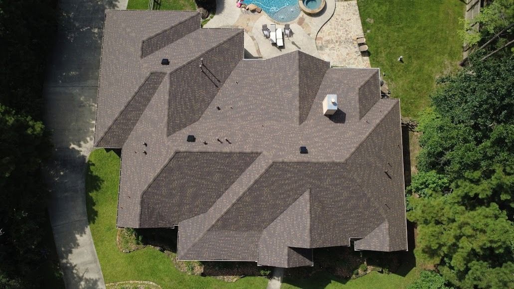 Aerial view of a suburban house with a brown shingled roof beside a backyard pool and trees