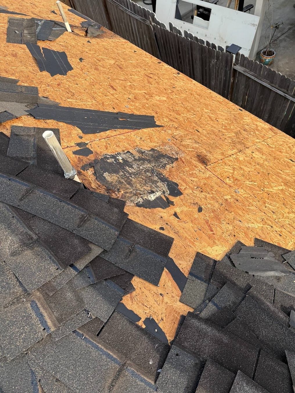 Damaged shingle roof with exposed orange underlayment and missing shingles near the peak