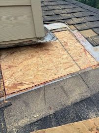 Roof with exposed plywood patch and damaged shingles around a vent or chimney base