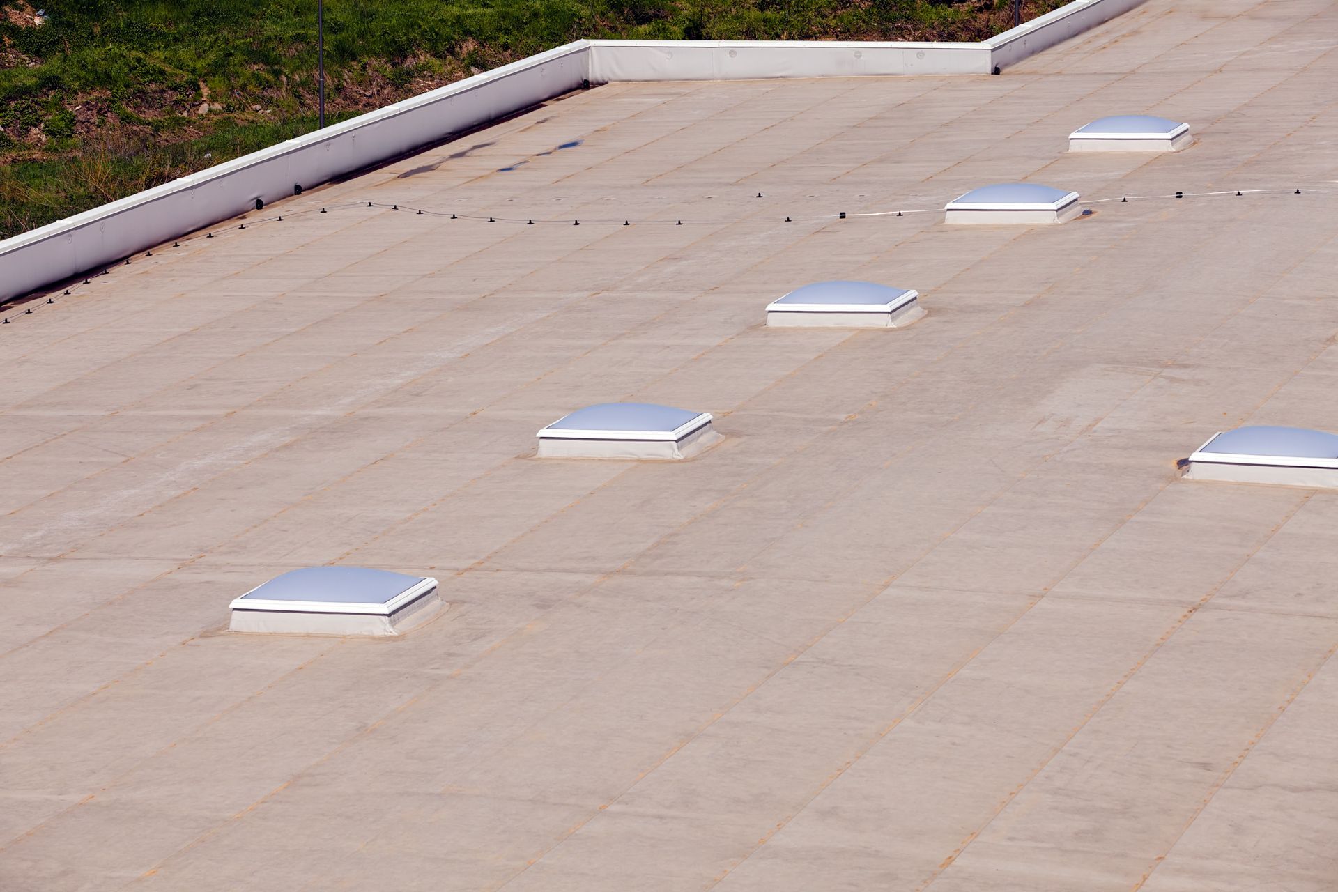 Flat beige rooftop with several white skylights and a low white parapet along the edge.