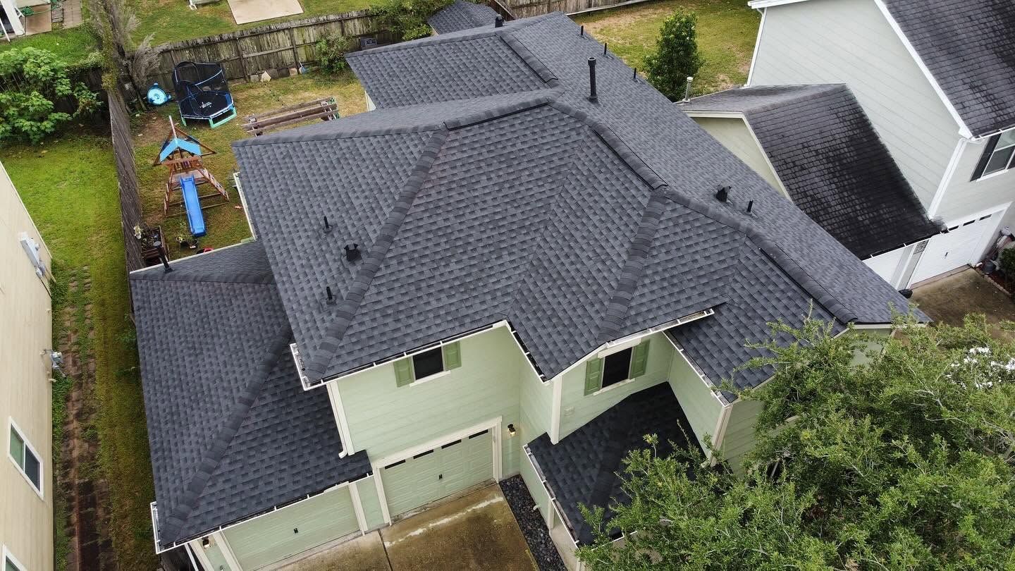 Aerial view of a house with a dark gray roof and small backyard bordered by fences and greenery.