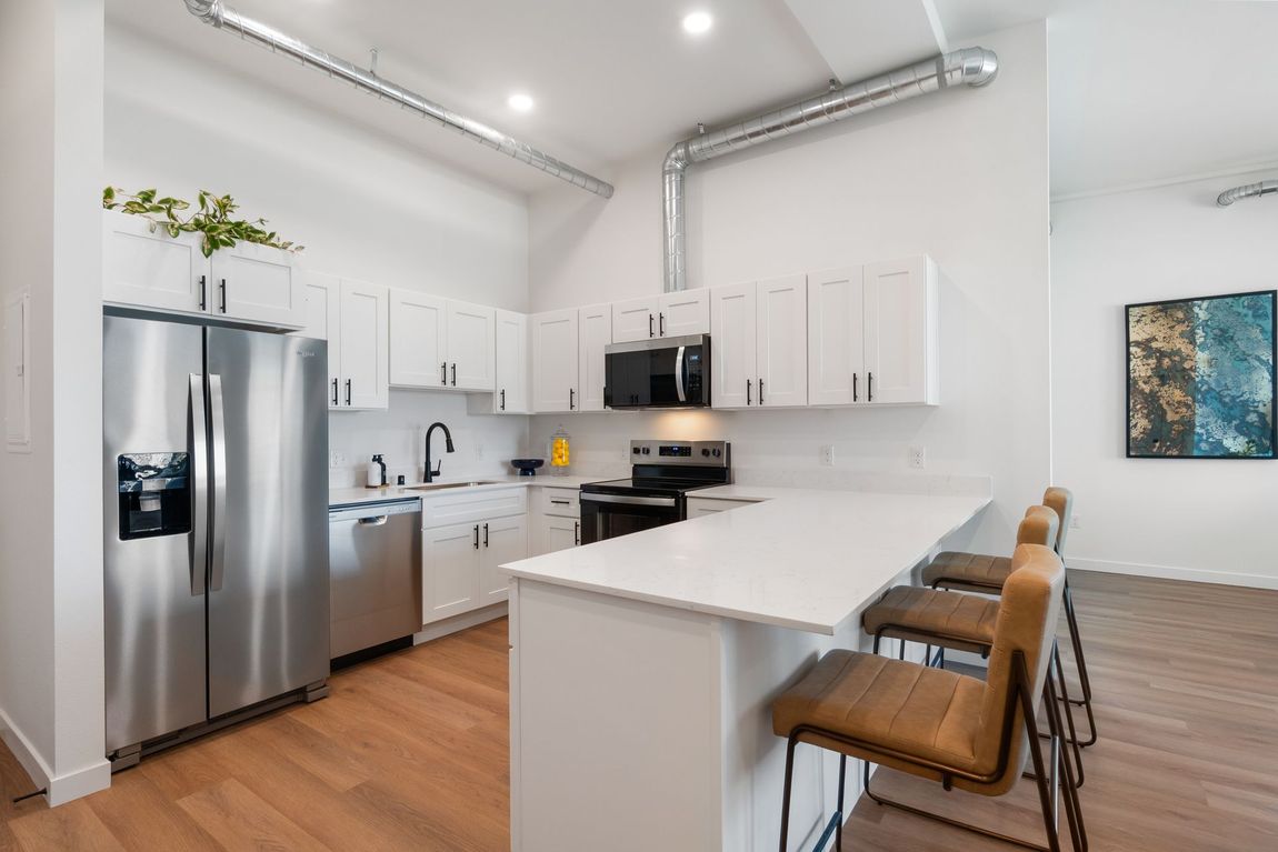Bright white kitchen with stainless steel appliances, marble counters, and a view into a cozy living area.