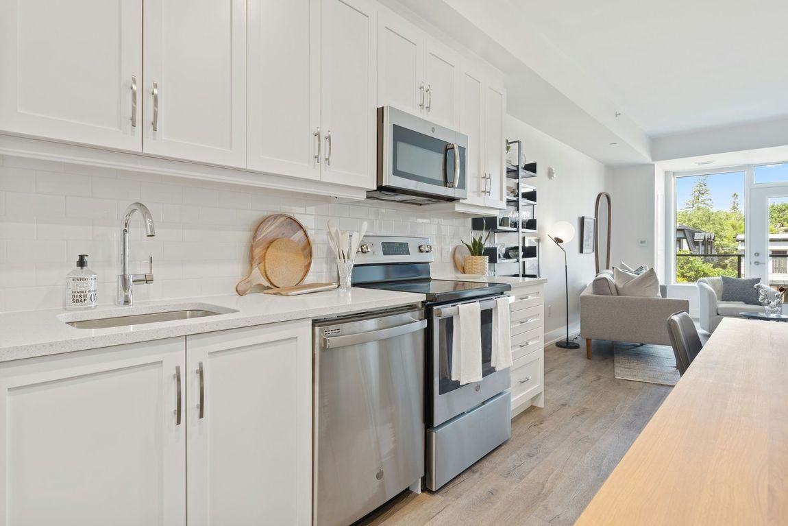 Bright white kitchen with stainless steel appliances, marble counters, and a view into a cozy living area.