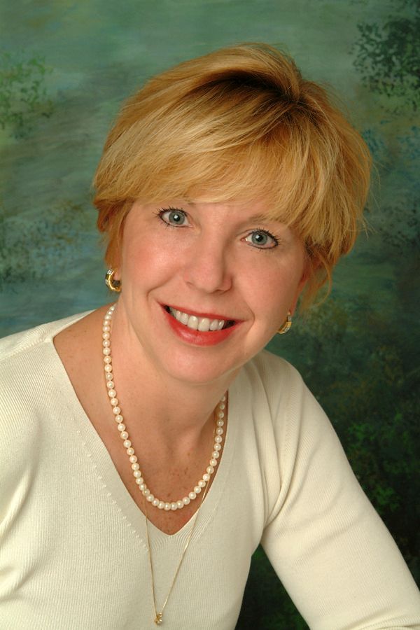 A woman wearing a pearl necklace and earrings is smiling for the camera.