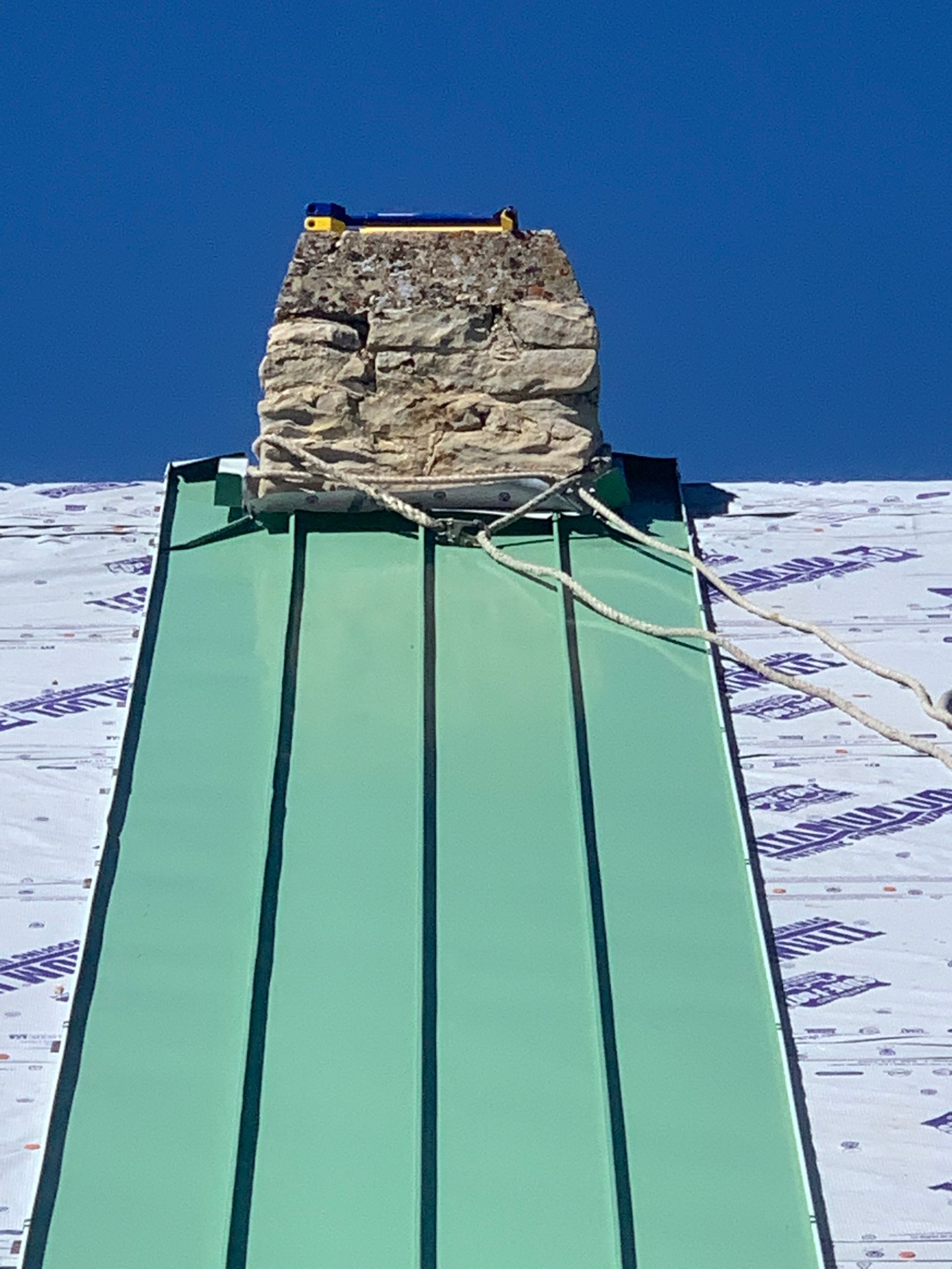 Green metal roof with a stone chimney against a snowy mountain sky