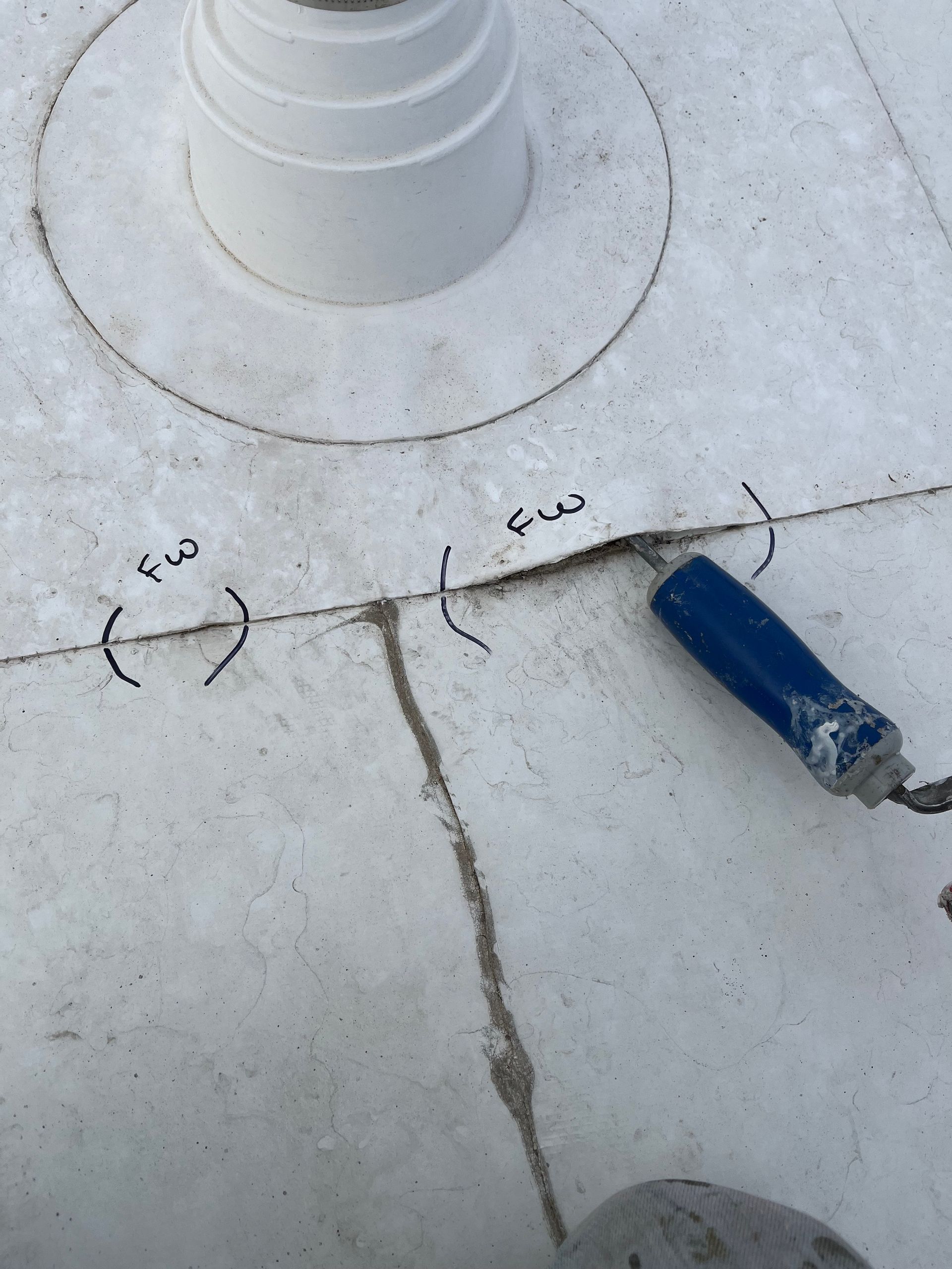 White concrete rooftop with a vent pipe, crack lines, and a blue marker tool.