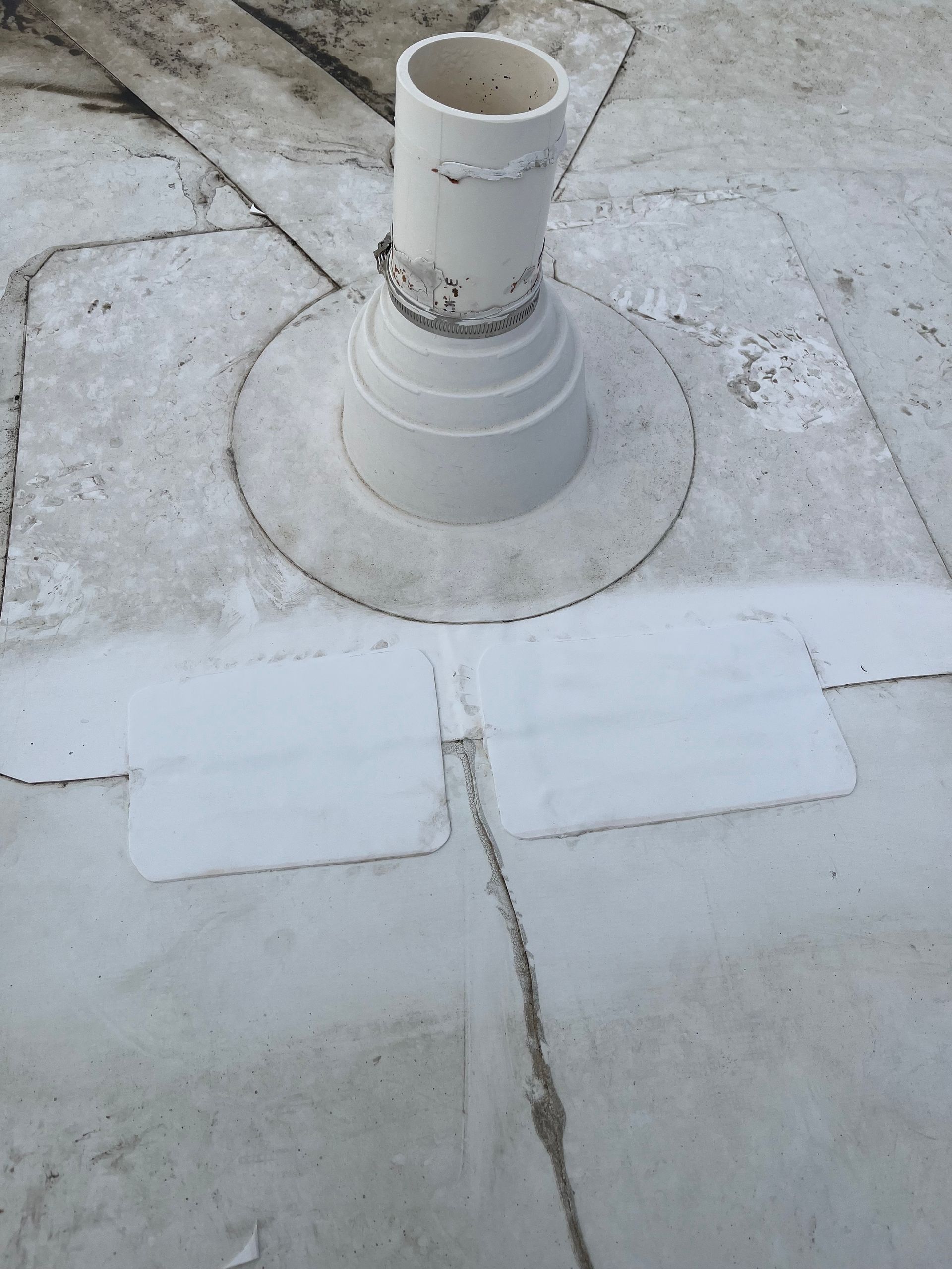 White rooftop vent pipe with sealed base and patches on a flat roof.