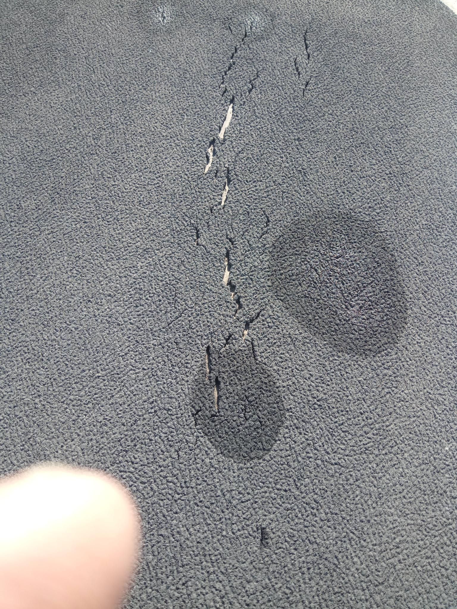Close-up of a gray textured surface with a dark stain or scratch and a fingertip at the bottom left.