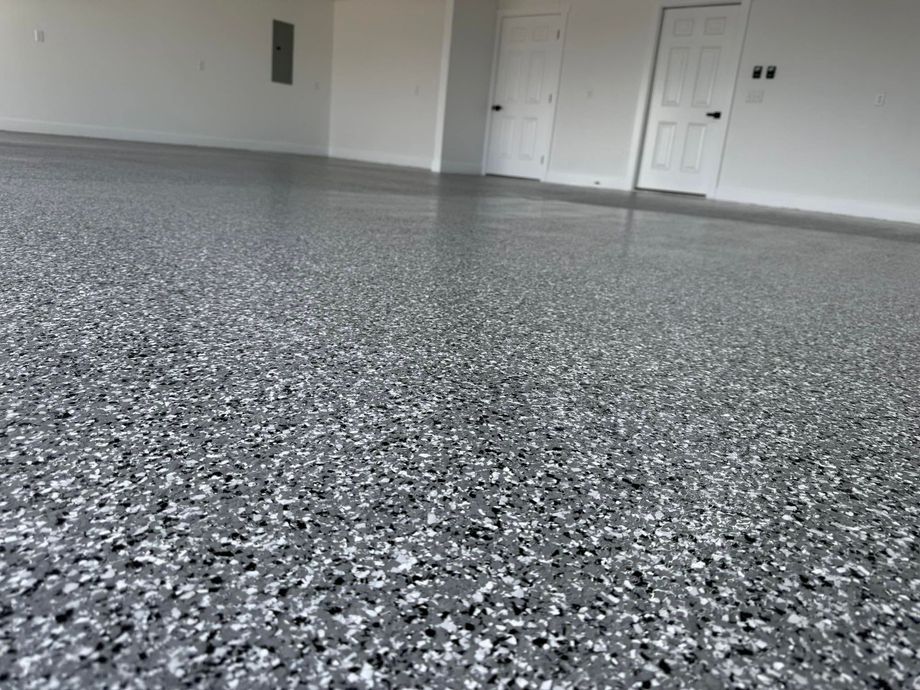Empty garage with gray speckled epoxy floor and white walls, viewed from low angle