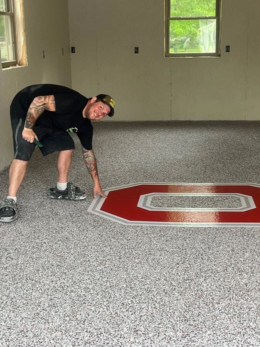 Person bent over marking a red octagonal shape on a speckled floor in an empty room