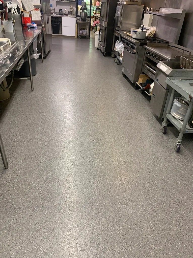 Commercial kitchen with stainless steel counters, equipment, and a gray speckled floor.