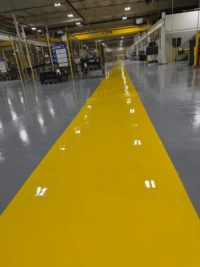 Yellow aisle line in a large industrial warehouse with polished gray floors and machinery in the background