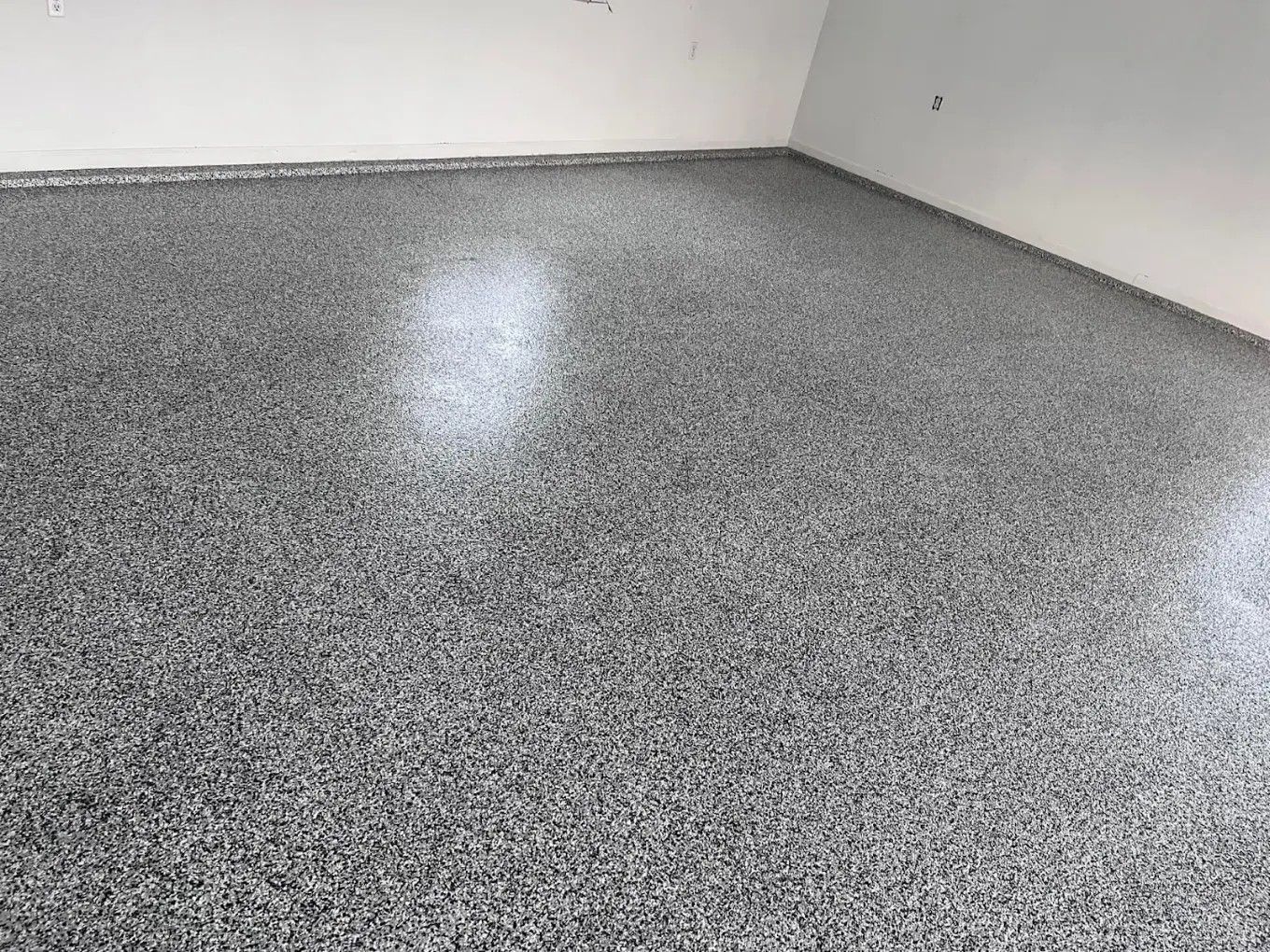 Empty speckled gray floor in a plain room with white walls and bright light reflections
