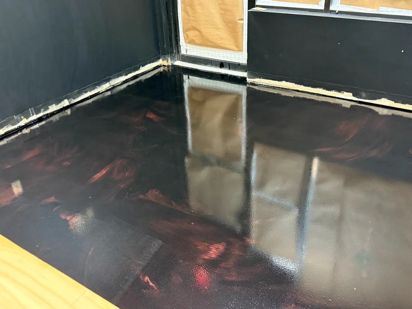 Glossy black floor in a dark corner room with a yellow doorway and wall reflections