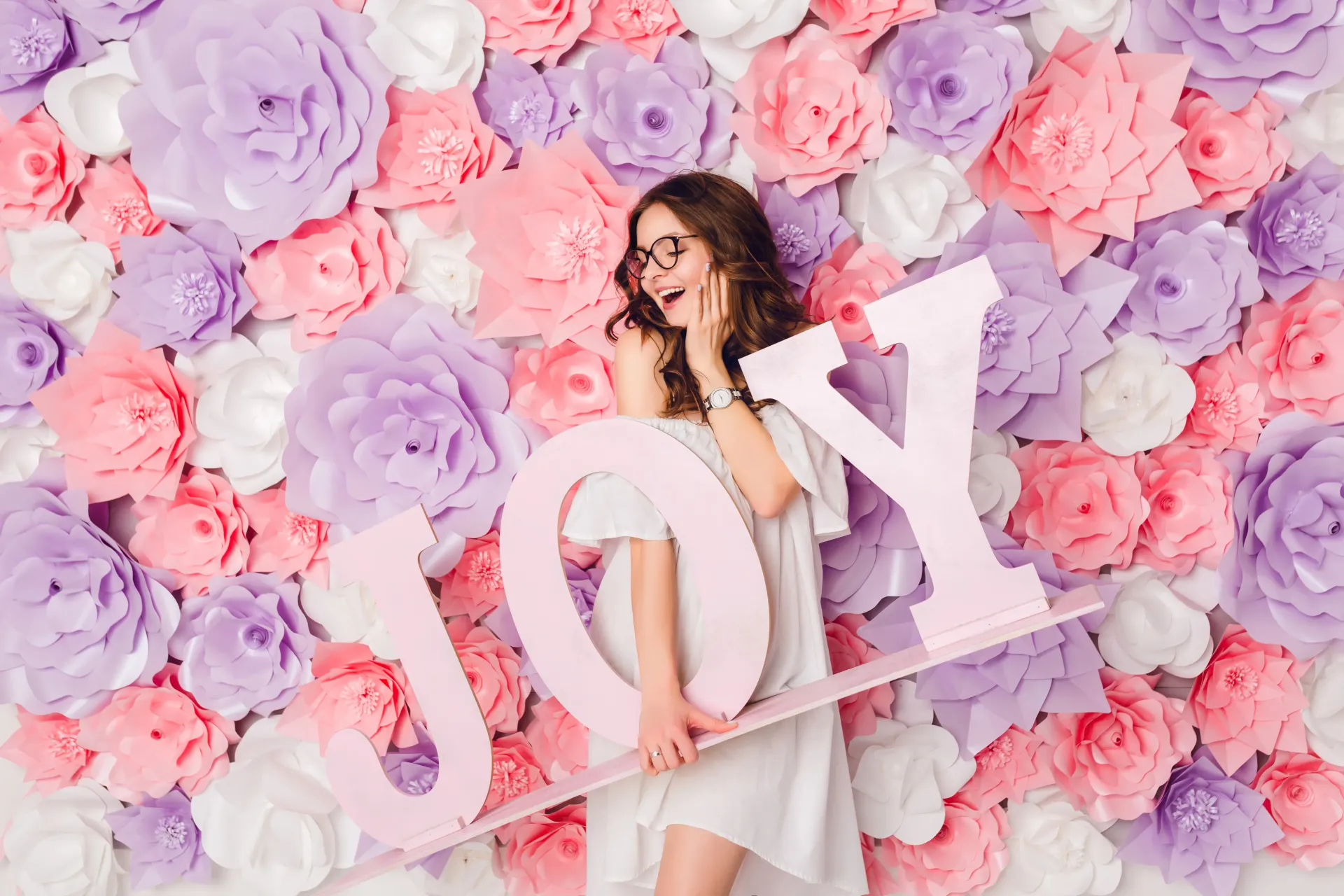 Anna is holding a sign that says joy in front of a wall of flowers in Philadelphia
