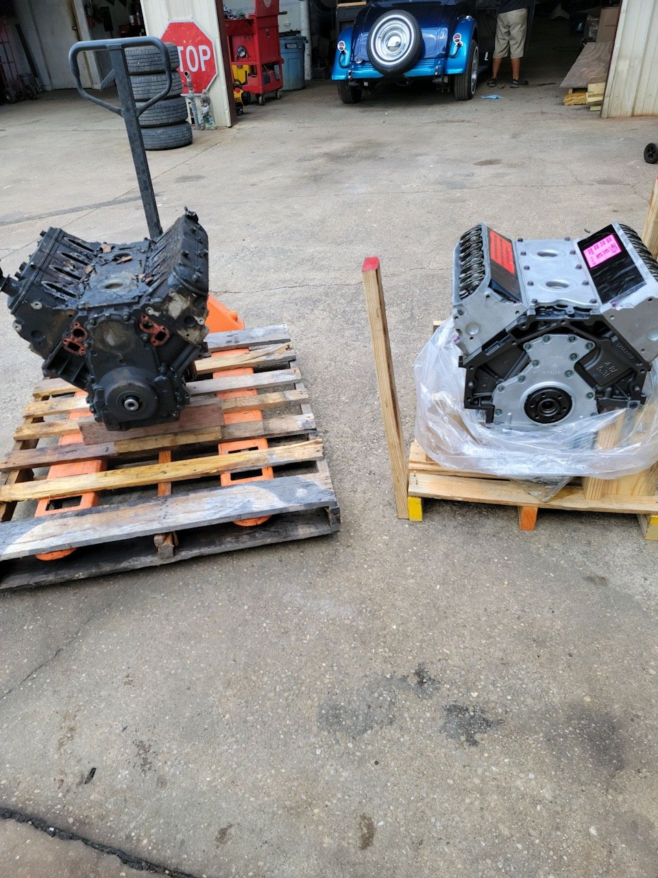 Two car engines on pallets sit outside a garage.