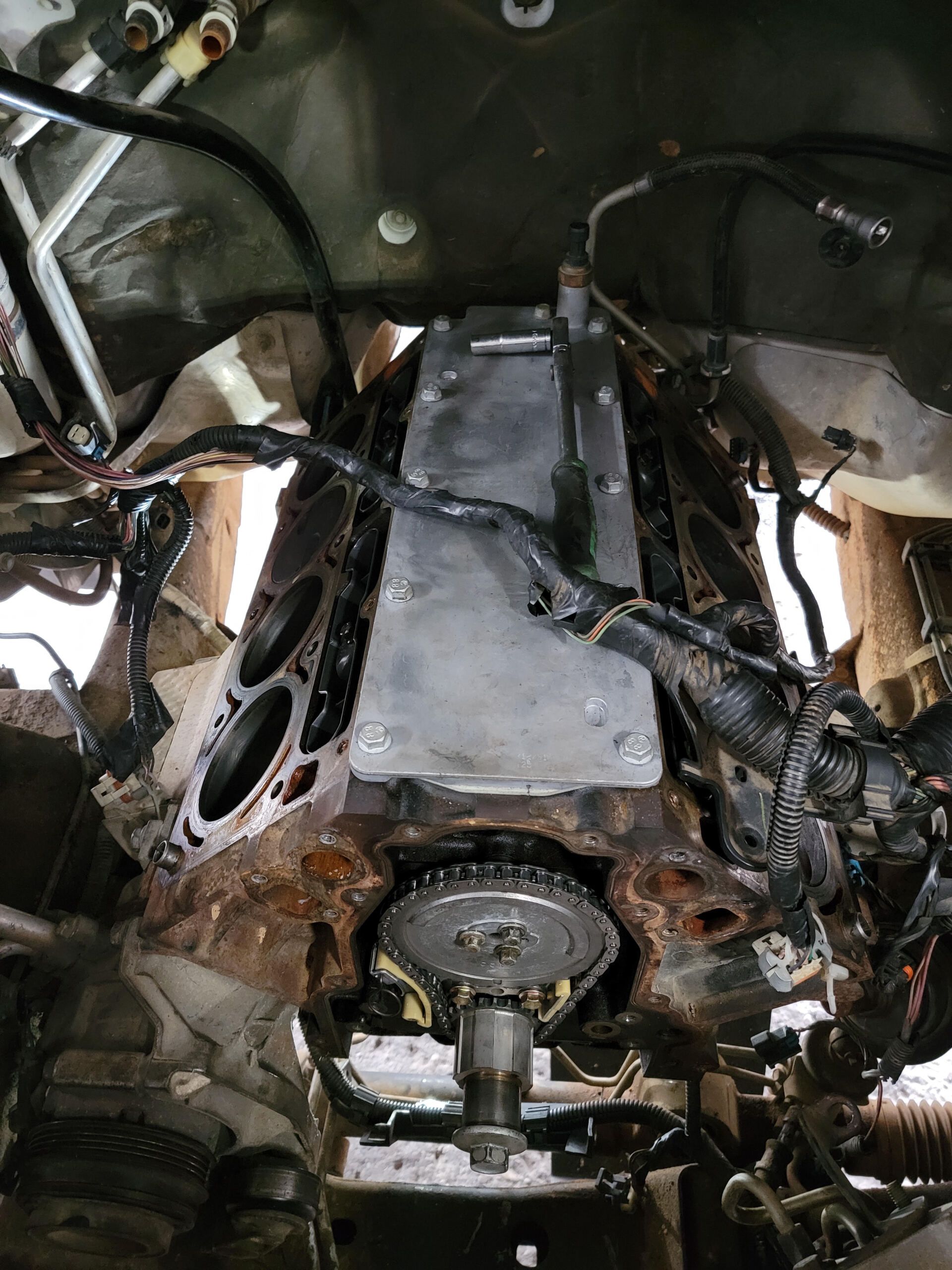 Engine block with timing chain visible, viewed from below, surrounded by components and wires.