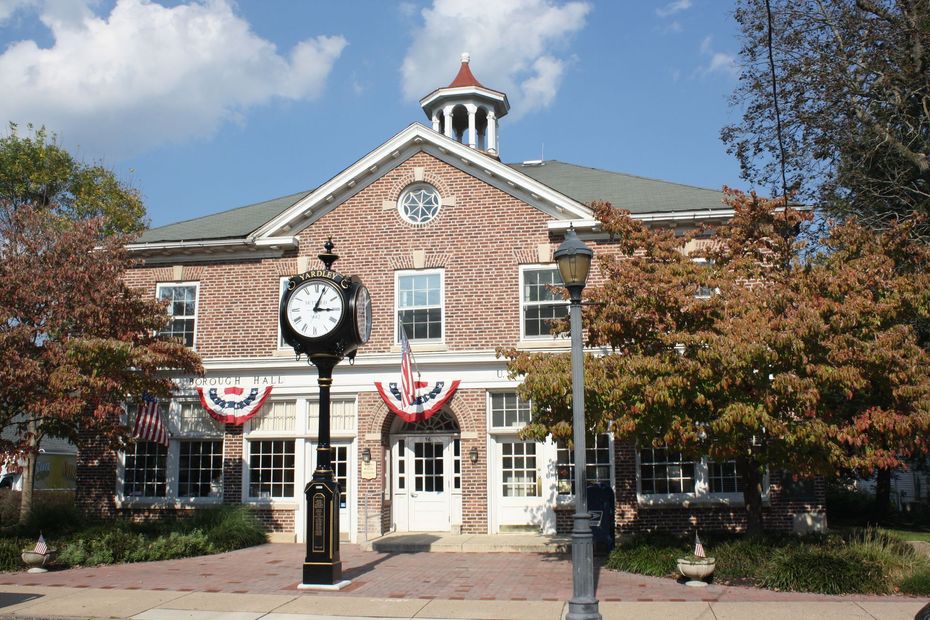Brick building with clock tower, flags, and fall foliage.