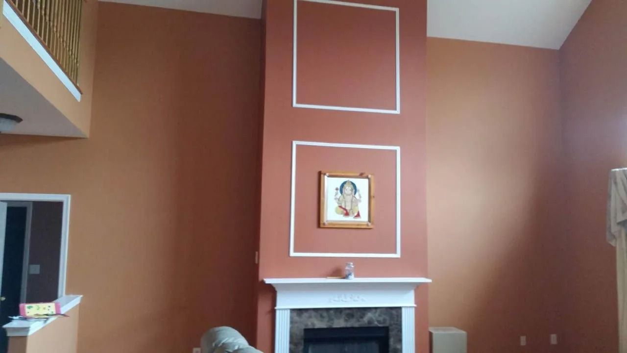 High-ceilinged living room with a fireplace, painted terracotta with white trim. A painting hangs above the mantle.
