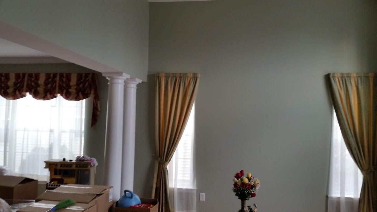 Interior of a room with sage green walls, white pillars, gold curtains, and a floral arrangement.