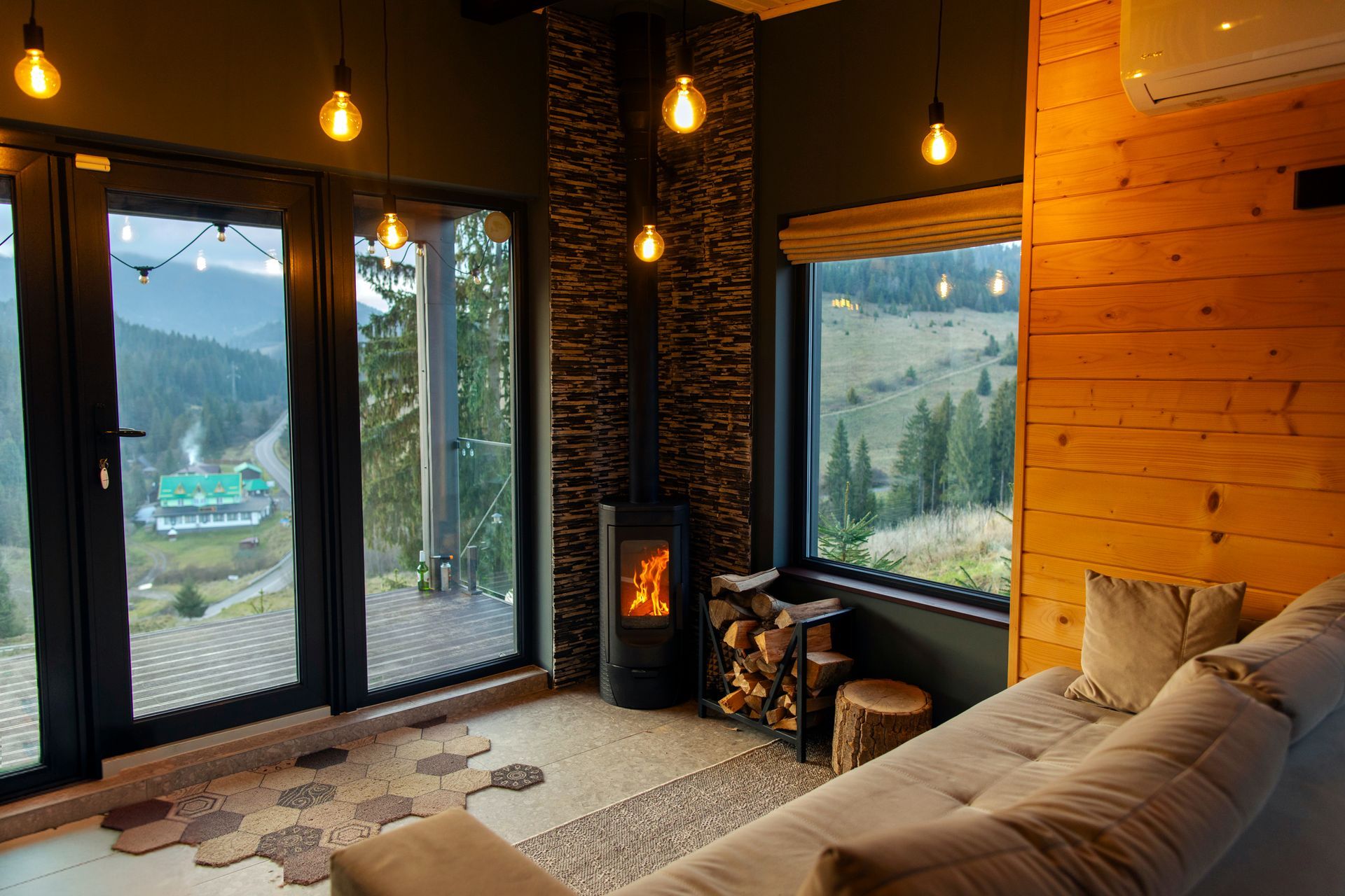 Cozy living room with fireplace, warm lights, large windows, and mountain view outside