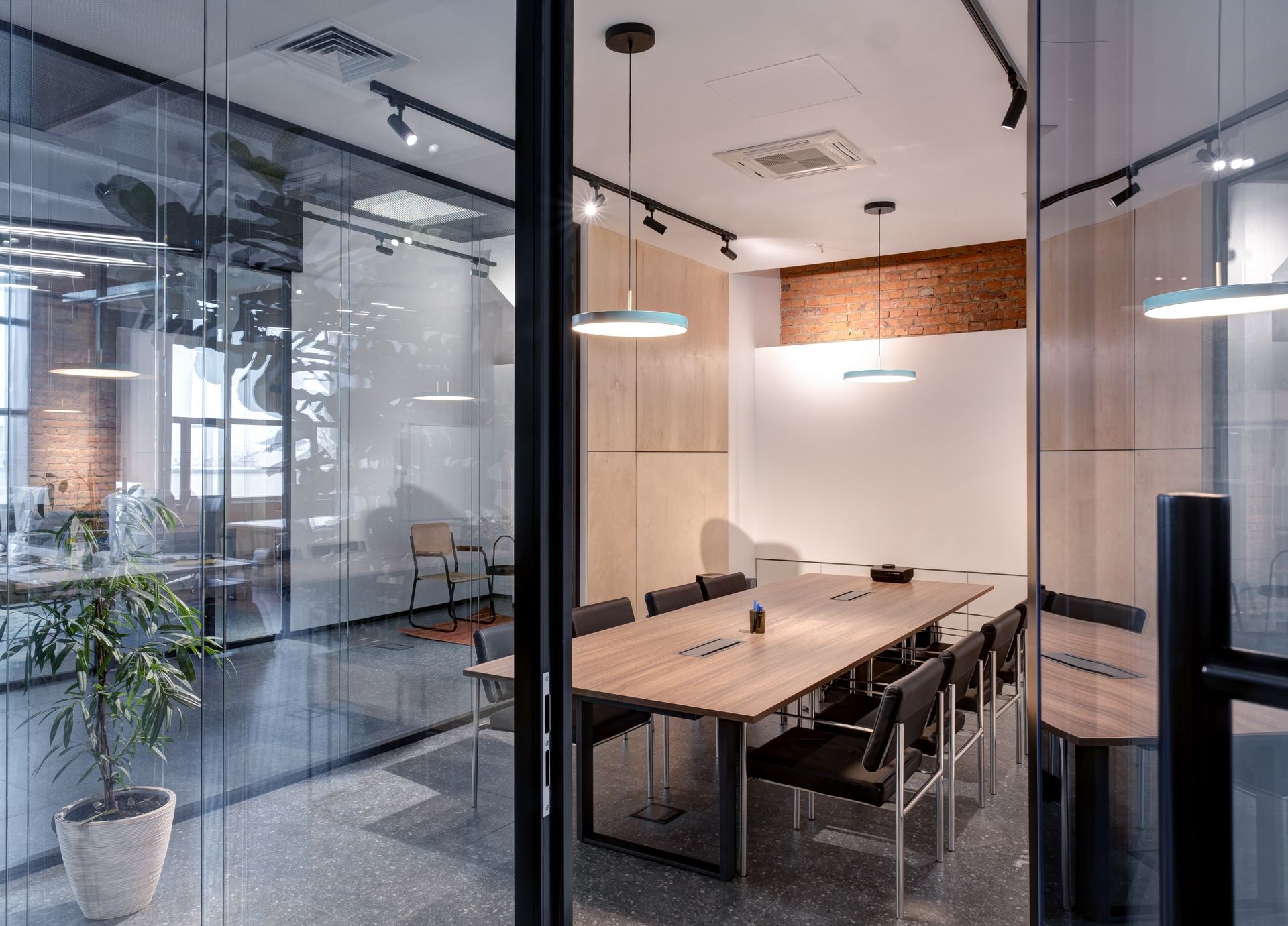 Modern glass-walled conference room with a long wooden table and pendant lights