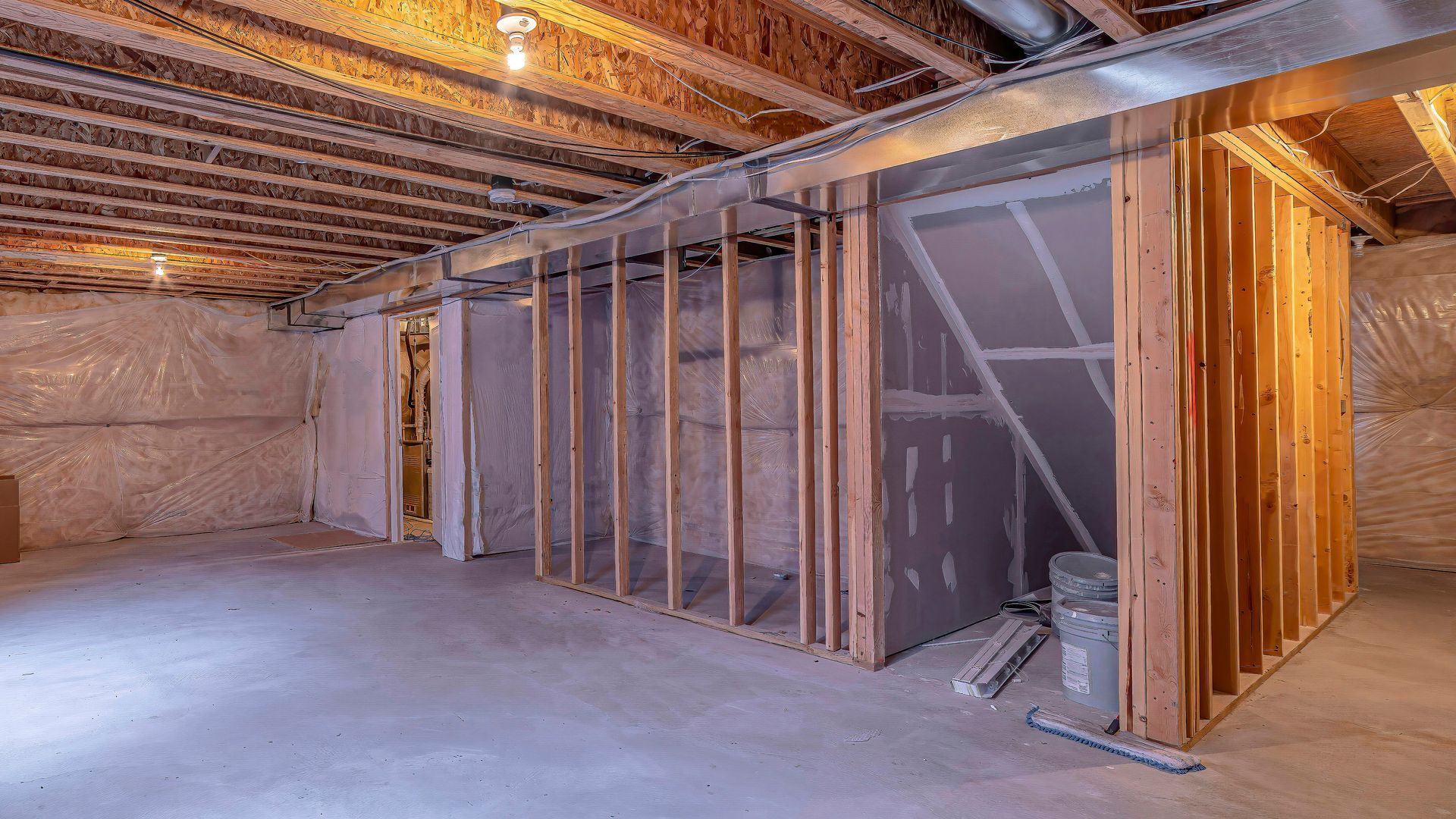 Unfinished basement with exposed wooden framing, insulated wall sections, and concrete floor