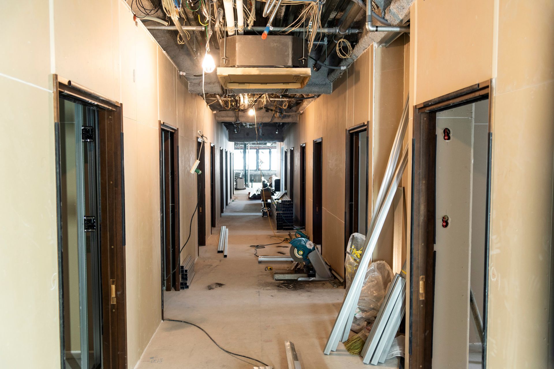 Partially finished office hallway with exposed ceiling, open doorways, and construction materials scattered on the floor