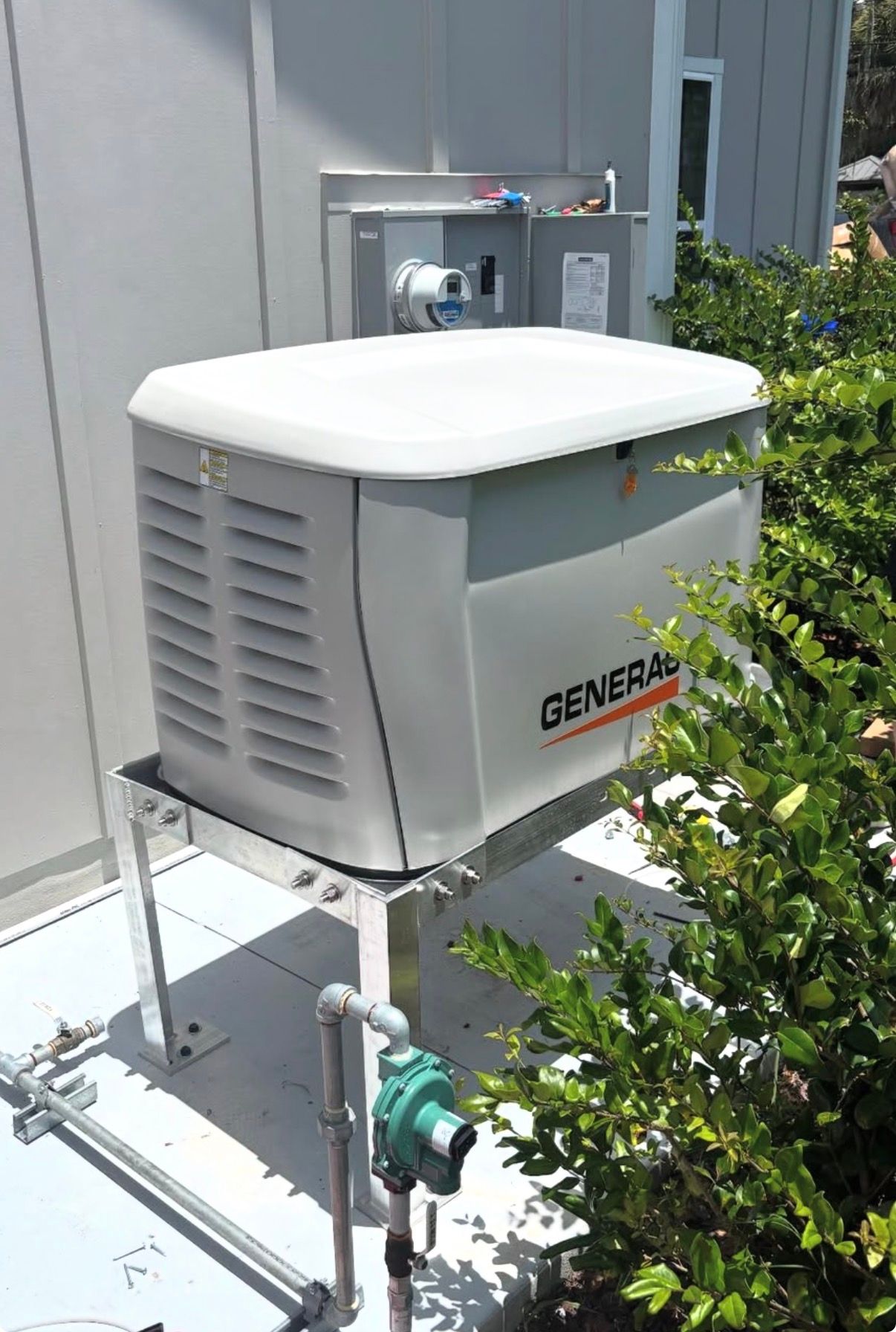 Outdoor generator unit beside a building, with white cover and metal piping.