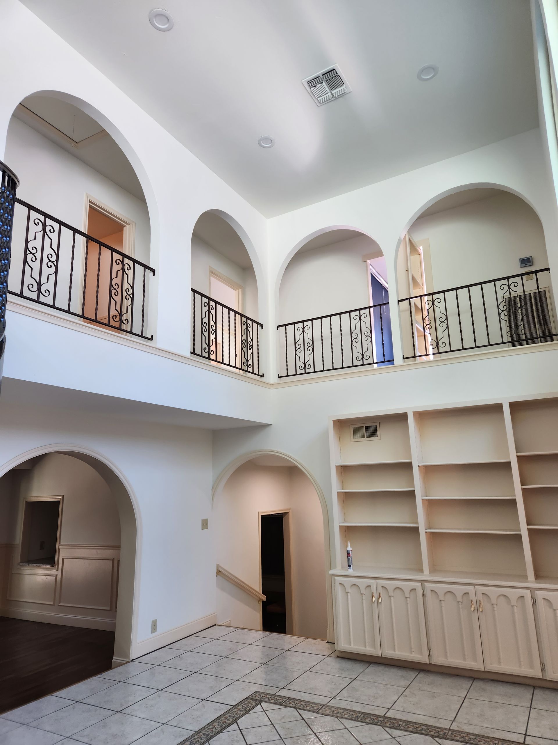 A two-story interior foyer with white walls, arched openings, black iron railings, and built-in shelving.