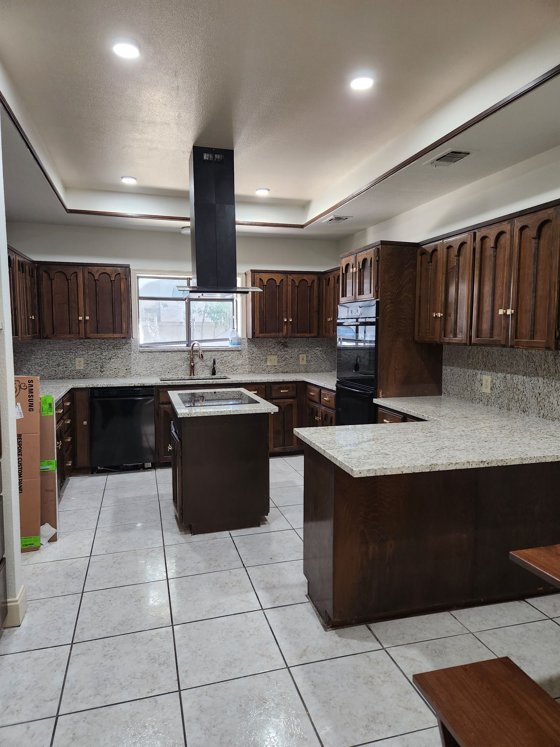 A kitchen with dark wood cabinets, speckled granite countertops, a center island, stainless appliances, and tile flooring.