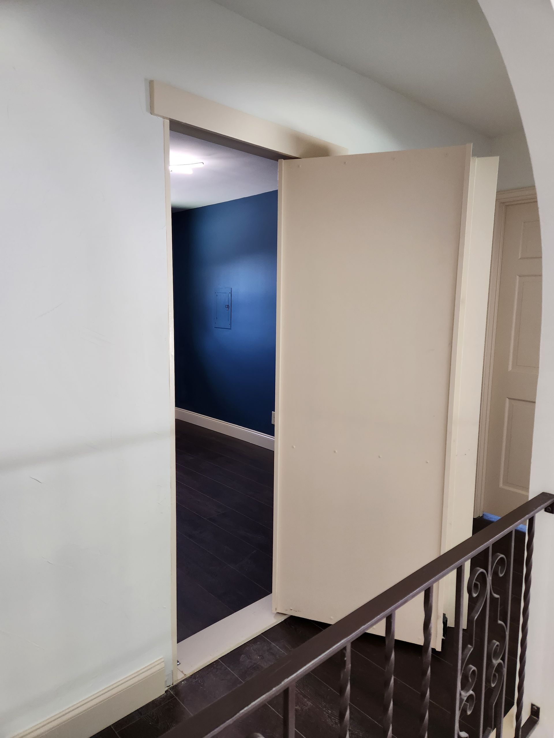 An open doorway reveals a room with dark blue walls and flooring, viewed from a landing with a dark metal railing.