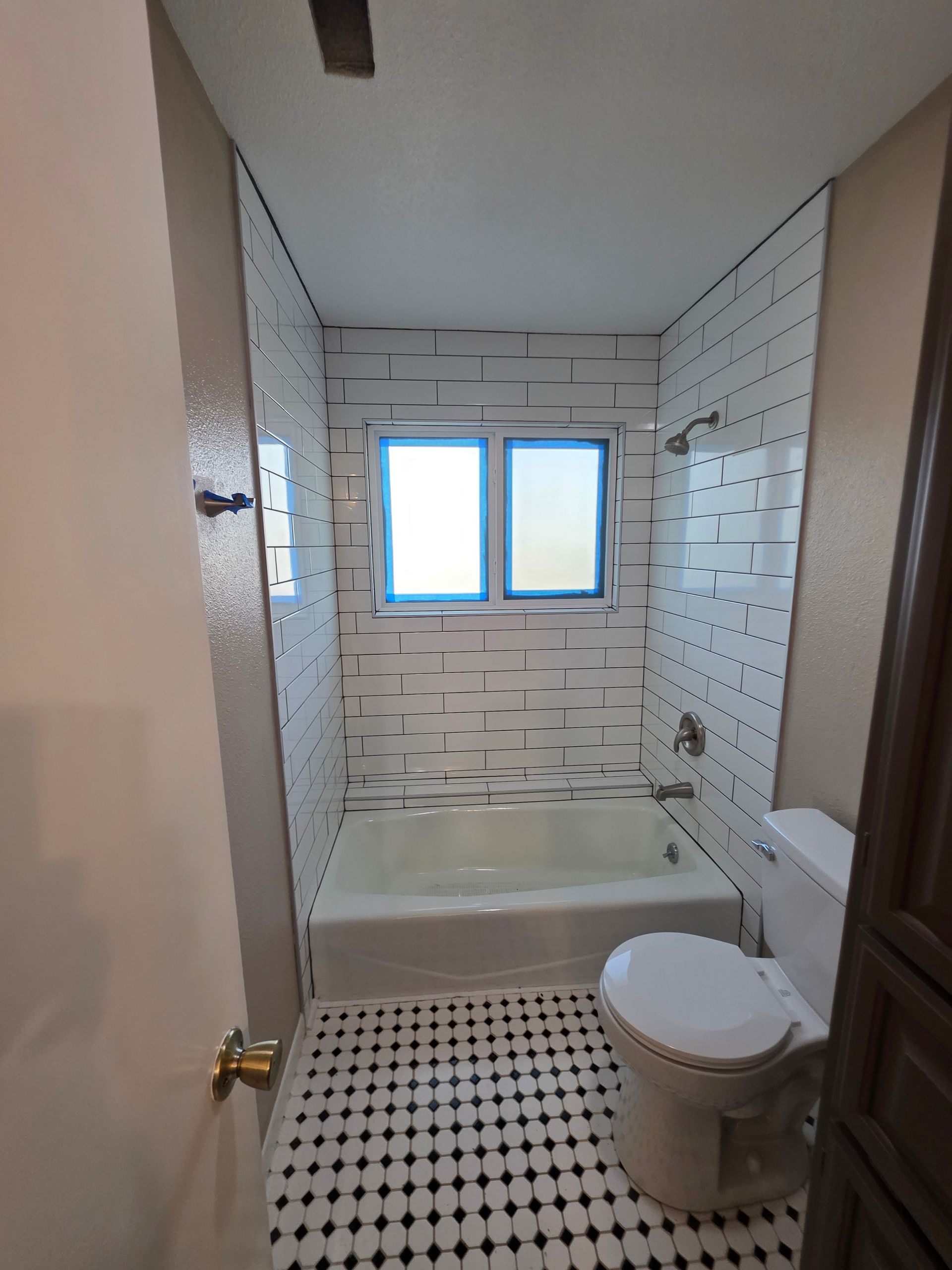 A bathroom featuring a white bathtub with subway-tiled walls, a window above the tub, and a black-and-white patterned floor.