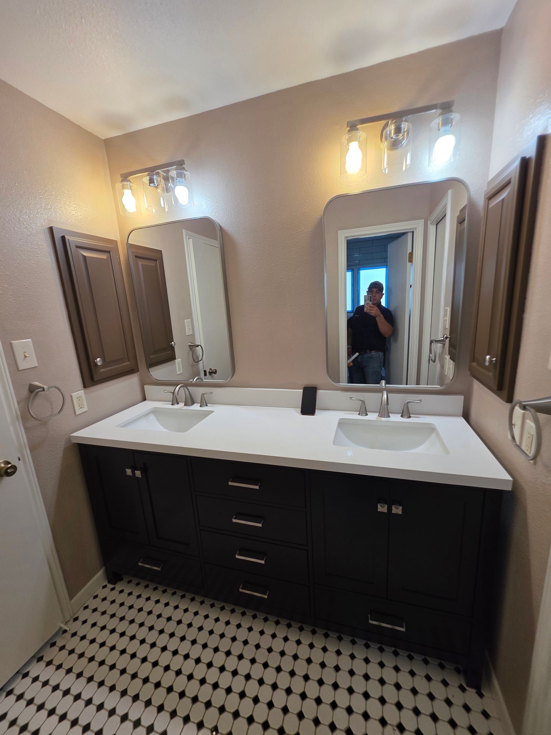 Double vanity with a white countertop, dark cabinets, two mirrors, and overhead lighting in a bathroom with tiled flooring.