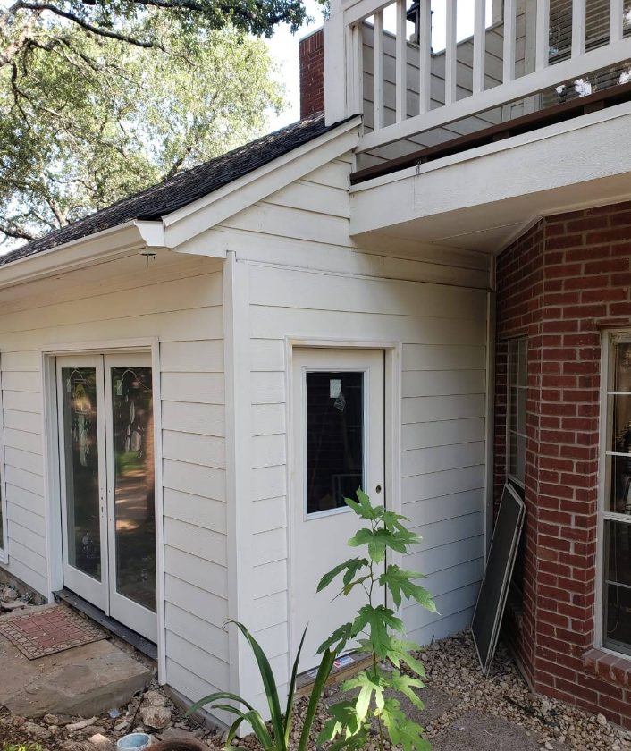 White home addition with French doors and a single door next to a brick section of a house with an upper balcony.