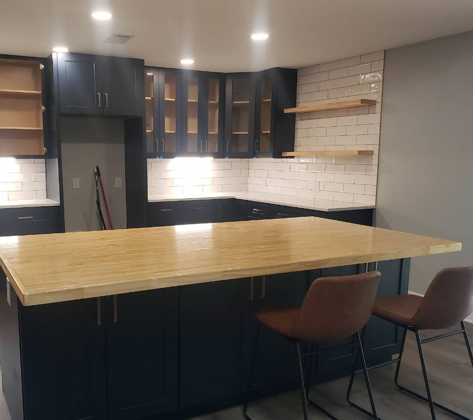 Modern kitchen with dark navy cabinets, a large light wood-topped island, stools, and white brick-style backsplash.