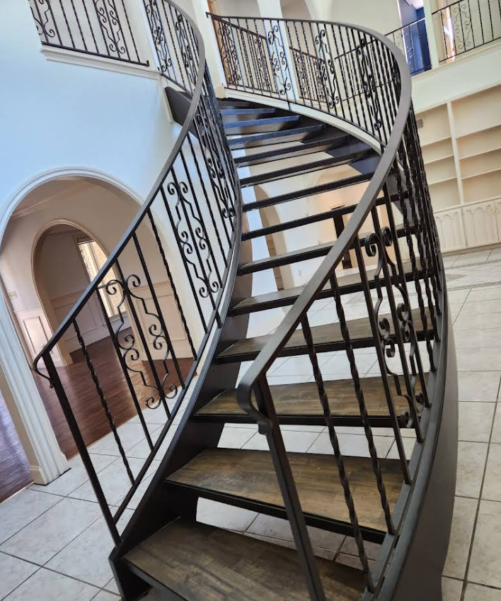 Curved staircase with dark wood treads and decorative wrought iron railings in a spacious, tiled interior.