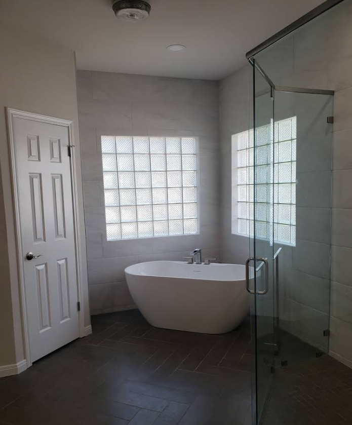 A modern bathroom featuring a white freestanding tub set between glass block windows, a glass shower, and a white door.