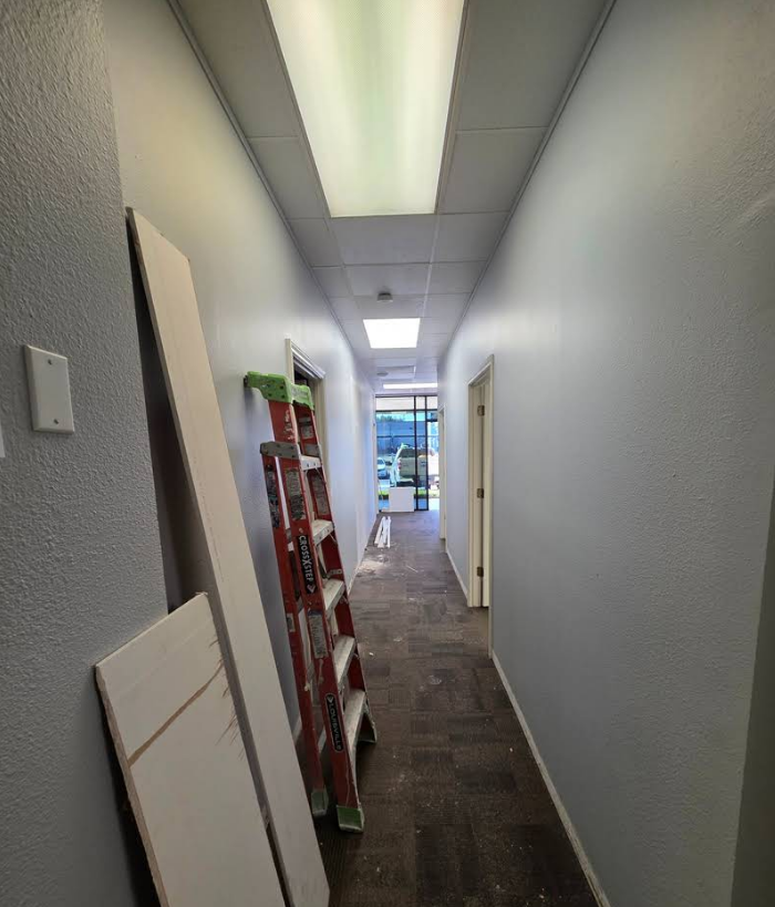 A long hallway with gray walls, a red ladder, and construction materials leaning against the left wall.