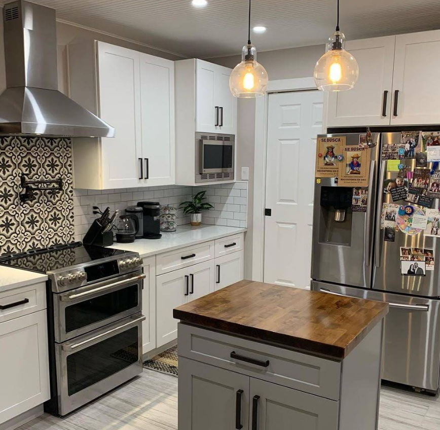 A kitchen featuring white cabinets, stainless steel appliances, a wooden island, and a decorative tile backsplash.