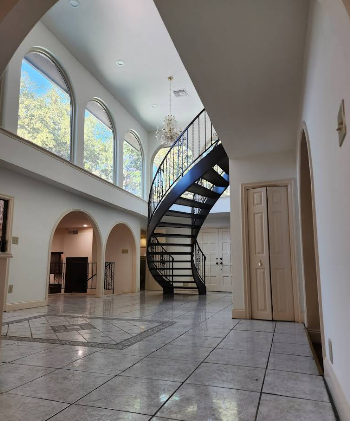 A modern foyer with white tiled floors, arched windows, and a prominent black spiral staircase leading to an upper floor.