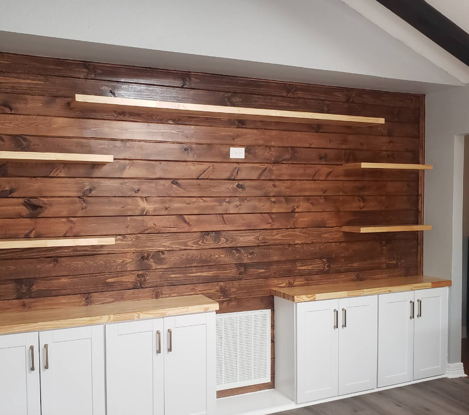 A rustic wooden accent wall with white base cabinets, floating shelves, and a built-in vent in a contemporary living space.