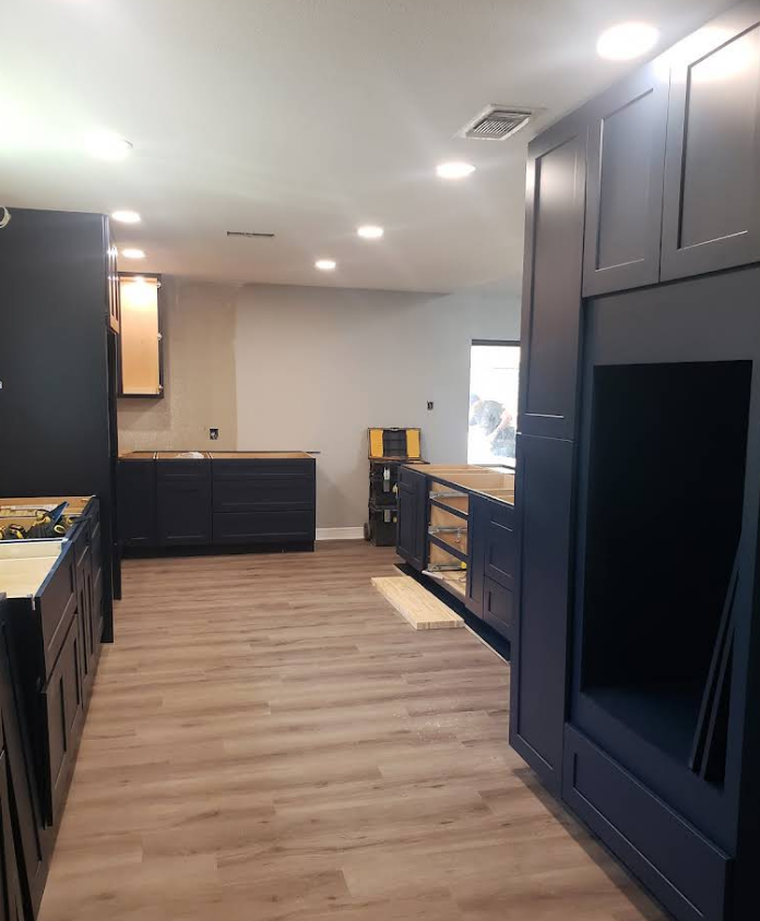An unfinished kitchen interior features dark blue cabinets, wood-look flooring, and recessed lighting.