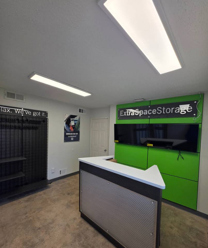 The interior of a storage facility office featuring a service counter, green back wall, display shelf, and security camera.